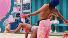 a man without a shirt is riding a woman in pink shorts and a blue hat .