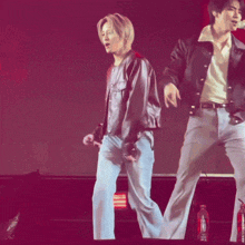 a man in a leather jacket is dancing on a stage with another man