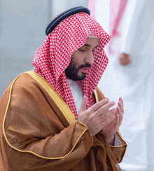 a man wearing a brown robe and a red and white checkered head scarf praying