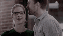 a man and a woman are standing next to each other and looking at each other . the woman is wearing glasses .