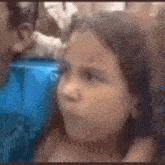 a little girl is making a funny face while sitting in a crowd of people .