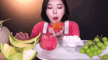 a woman in a red shirt is eating a peach surrounded by melons and grapes