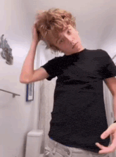 a young boy in a black shirt is standing in a bathroom with his hand in his hair .