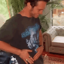 a man wearing a black t-shirt with a picture of a man on it is standing next to a couch