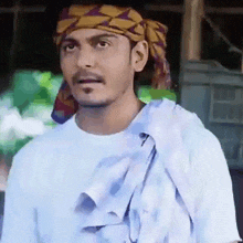 a man wearing a turban and a white shirt looks at the camera .