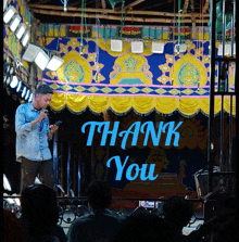a man singing into a microphone in front of a thank you banner