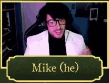 a man with glasses and headphones is sitting in front of a green board that says mike ( he )