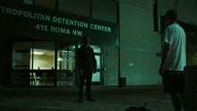 two men standing in front of a building that says metropolitan detention center 415 roma nw