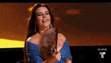 a woman in a blue dress is holding a fan and smiling on a stage .