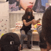 a woman wearing a mask is sitting on a couch in front of a poster that says wish you