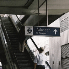 a man is walking up an escalator next to a blue sign that says to resign .