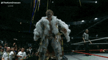 a man in a white feathered coat stands in front of a crowd with the words " thekamdreesen " on the bottom