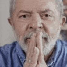 a man with a beard and a blue shirt is praying with his hands folded .