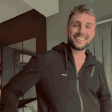 a man with a beard is smiling and wearing a black hoodie