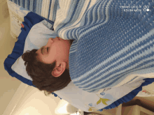 a boy laying on a bed with a blue blanket and a redmi note 8 camera