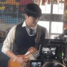 a young man in a vest and tie is playing a guitar in front of a camera .