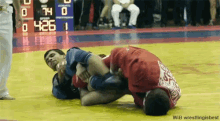 two men are wrestling on a wrestling mat with a scoreboard behind them that says 74 0 425 1