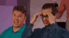 two men are sitting next to each other and one of them is wearing glasses and making a funny face .