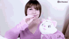 a woman in a pink shirt is holding a stuffed cat and a glass of water .
