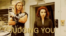 a man and a woman are standing next to each other in a room with the words judging you written on the wall .