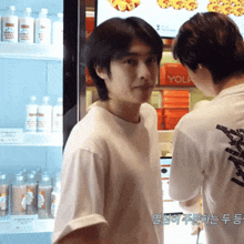 a man in a white shirt stands in front of a fridge with bottles of milk on it