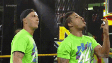 two men in green shirts are standing next to each other in a ring .