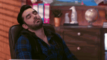 a man in a blue and black plaid shirt is sleeping in a chair
