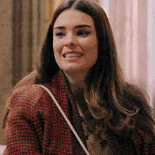 a woman wearing a plaid jacket and a white purse smiles