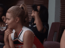 a cheerleader wearing a red white and blue top with the letter c on it is sitting next to another woman