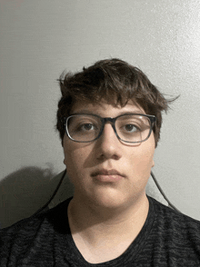 a young man wearing glasses and a black shirt stands in front of a white wall