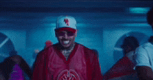 a man wearing a red jersey and a baseball cap is standing in a dark room .