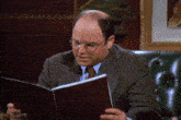a man in a suit and tie is sitting in a chair reading a book .