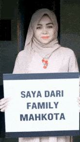 a woman in a hijab holds up a sign that says saya dari family mahkota
