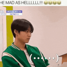 a man in a green jacket is sitting in front of a sign that says he mad as hell