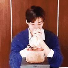 a man in a blue sweater is eating a birthday cake