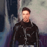 a man wearing a black leather jacket is standing in front of a wall