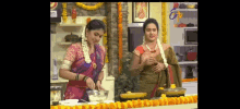 two women are preparing food in a kitchen with flowers on the wall