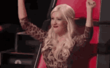 a blonde woman is sitting in a chair with her arms in the air .