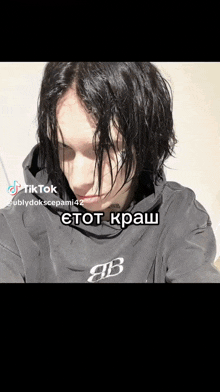 a man with black hair is wearing a black hoodie with a b on it