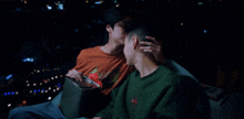 a man wearing a green sweatshirt with a flower on it kisses another man 's forehead