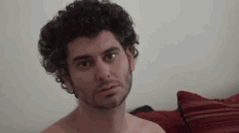 a shirtless man with curly hair and a beard is looking at the camera .