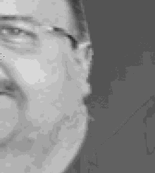 a close up of a man 's face wearing glasses and smiling in a black and white photo .
