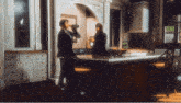 a man in a suit drinks from a bottle while standing in a kitchen
