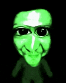 a green face with black eyes and a tongue sticking out
