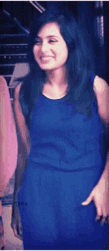 a woman in a blue dress is smiling and pointing at the camera