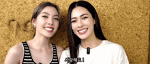 two women are standing next to each other and smiling in front of a wall with korean writing on it