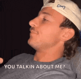 a man wearing a hat and a gray shirt is sitting on a couch and talking to someone .