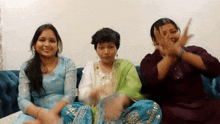 three women are sitting on a couch with their hands up