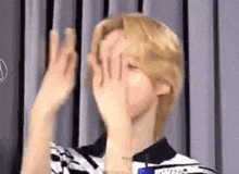 a man with blonde hair is covering his face with his hands and making a funny face .