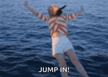 a woman in a striped shirt and white shorts is jumping in the water .